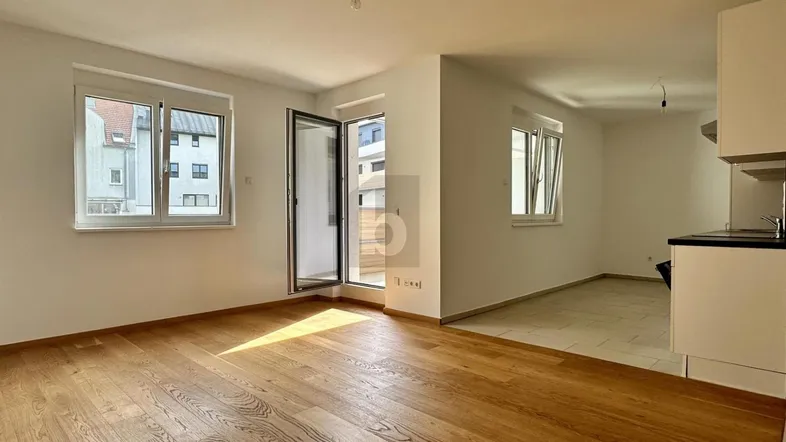 Helles, offenes Wohnzimmer mit Holzboden und Zugang zu einem Balkon oder einer Terrasse.