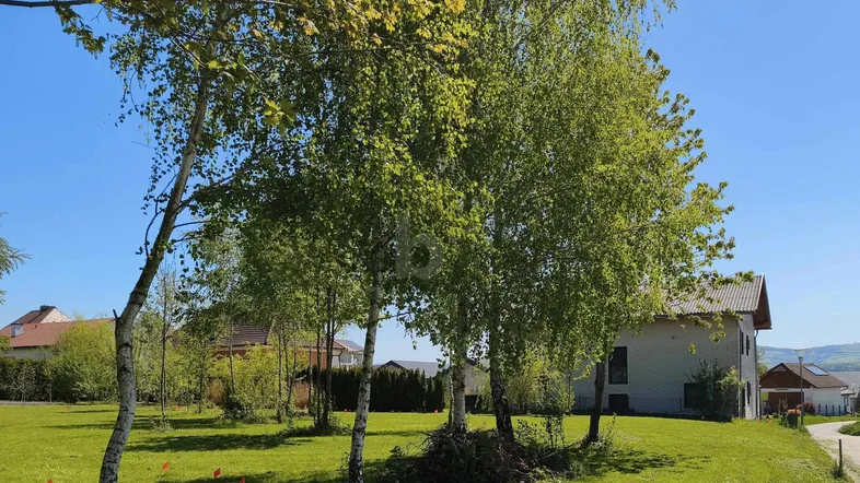 Großer Garten mit jungen Bäumen und Blick auf die umliegende Landschaft und ein Wohnhaus.