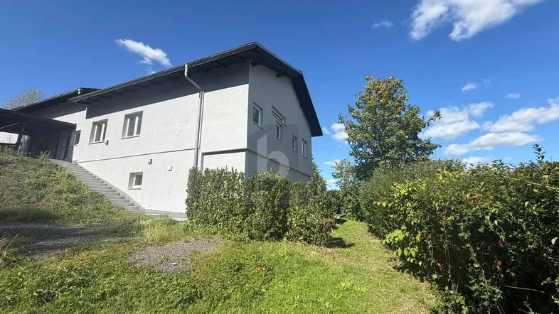 Außenansicht eines modernen Hauses mit grauer Fassade und grüner Umgebung unter blauem Himmel.
