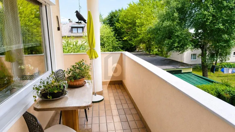 Helles Balkon mit Fliesenboden, einem kleinen Tisch und weitem Blick ins Grüne.