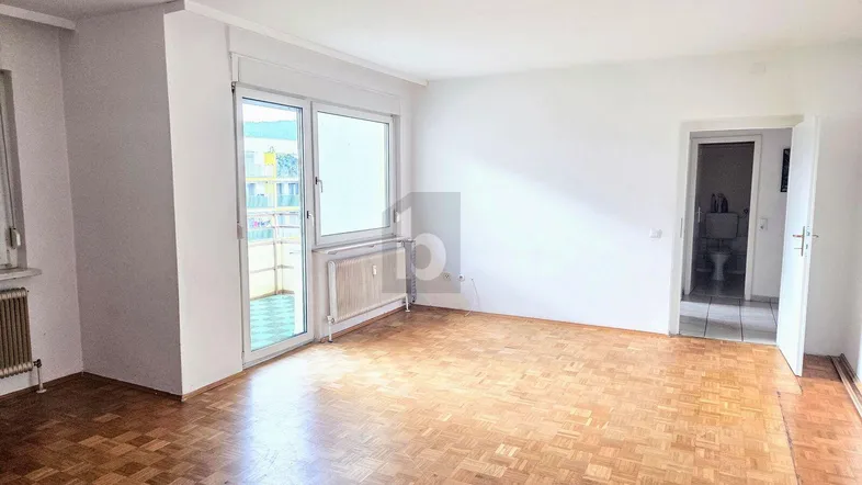 Helles Wohnzimmer mit Parkettboden, Zugang zum Balkon und Blick in ein angrenzendes Badezimmer.