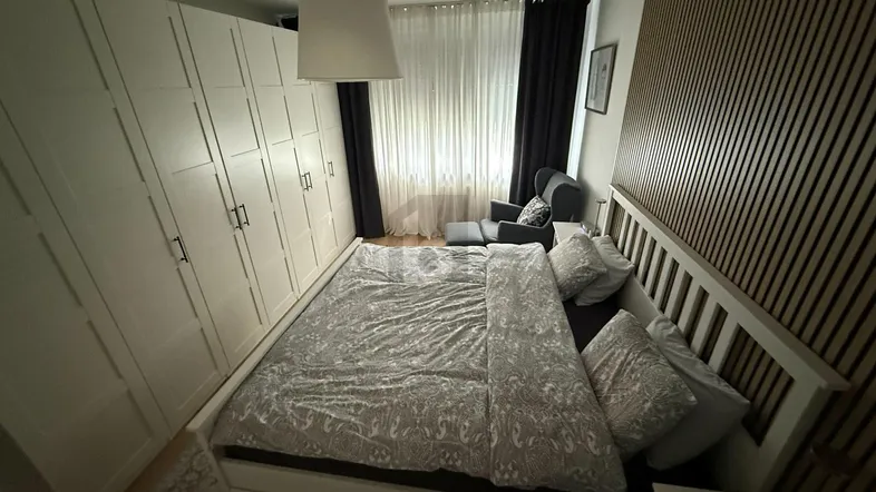 Helles Schlafzimmer mit großem Kleiderschrank, Doppelbett und moderner Holzwandverkleidung.