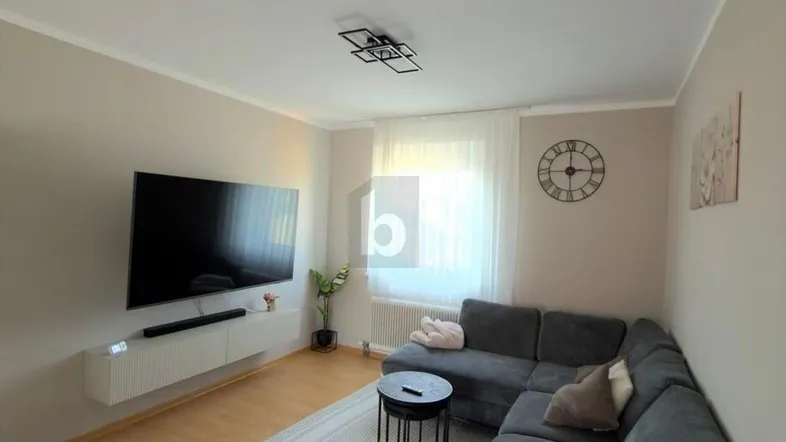 Modernes Wohnzimmer mit großem Ecksofa, Flachbildfernseher und hellem Parkettboden.
