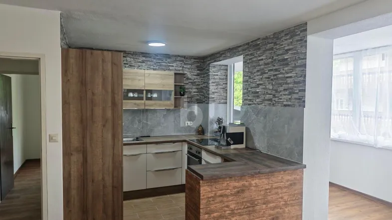 Moderne Küche mit Holzoptik-Schränken, Steinwand-Akzenten und offener Theke zum Wohnbereich.