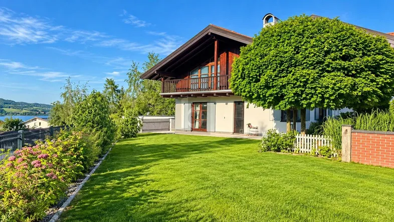 Charmantes Haus mit gepflegtem Rasen und Balkon, umgeben von grüner Natur und mit Seeblick.