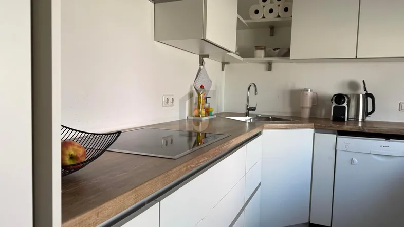 Moderne Küche mit weißen Schränken, Holz-Arbeitsplatte, Induktionskochfeld und integriertem Geschirrspüler.