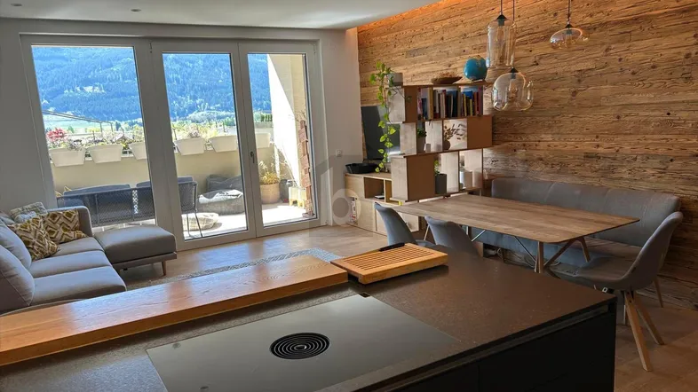 Moderner offener Wohnbereich mit Holzwand, integrierter Küche und Zugang zu einem Balkon mit Bergblick.