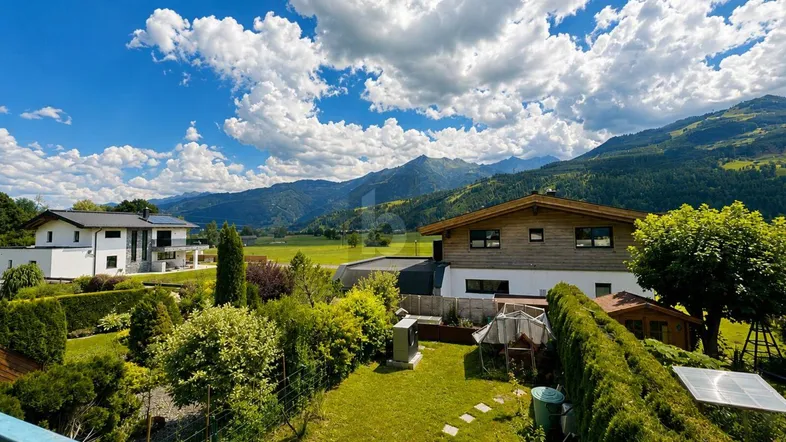 Gepflegter Gartenbereich mit Rasenfläche und Hecken, umgeben von einer malerischen Berglandschaft.