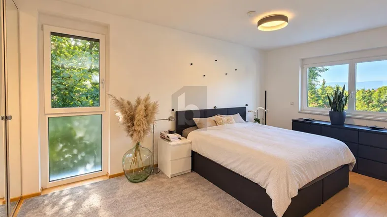 Helles Schlafzimmer mit Holzboden, großem Fenster und Blick ins Grüne, ausgestattet mit modernen Möbeln.