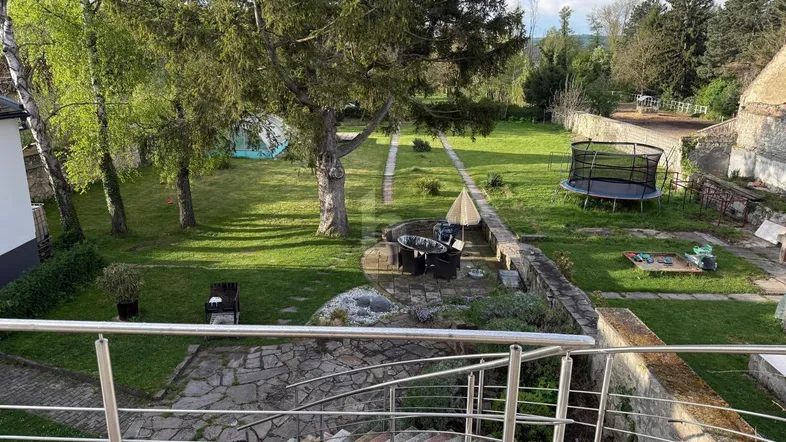 Großer Garten mit Rasenflächen, altem Baumbestand, Sitzbereich und Trampolin.