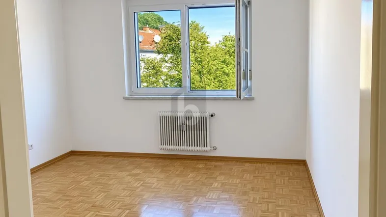 Helles Zimmer mit Parkettboden und Fensterblick ins Grüne, ideal als Schlaf- oder Arbeitszimmer.