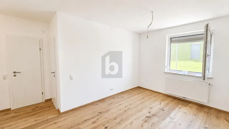 Helles Zimmer mit Holzboden und Fenster, bereit zur individuellen Gestaltung und Nutzung.