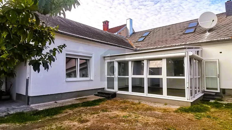 Außenansicht des Hauses mit einem verglasten Wintergarten und trockenem Rasenbereich.