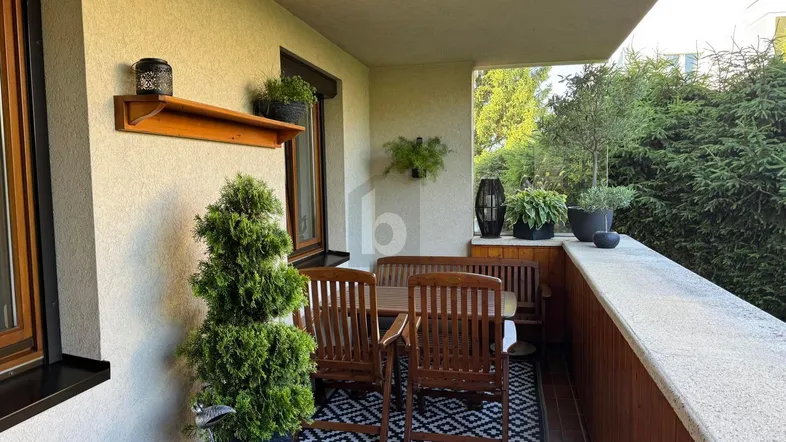 Gemütlicher Balkon mit Holztisch und Stühlen, umgeben von Pflanzen und mit Blick ins Grüne.