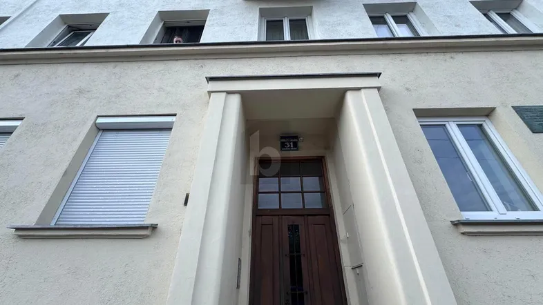 Die Fassade eines Mehrfamilienhauses mit beiger Putzfassade, Fenstern und Rollläden, die auf eine gepflegte Immobilie hindeuten.