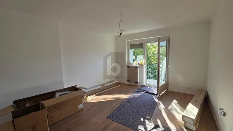 Helles Wohnzimmer mit neuem Laminatboden und Zugang zu einem kleinen Balkon, derzeit im Umbau.