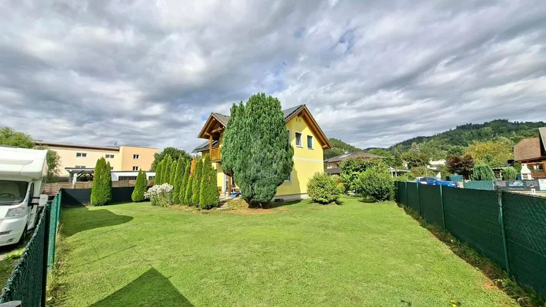Großer grüner Garten mit Rasenfläche und einem gelben Einfamilienhaus im Hintergrund.