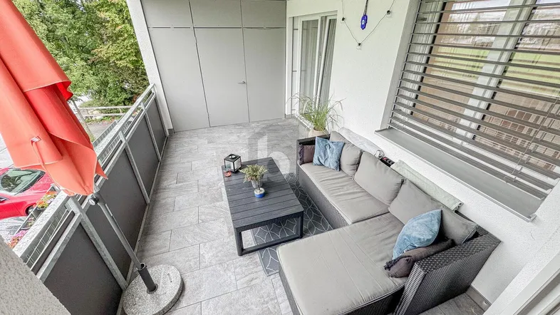 Geräumiger Balkon mit modernen Fliesen, bequemen Loungemöbeln und einem Sonnenschirm für entspannte Stunden im Freien.
