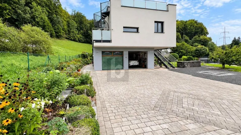 Modernes Haus mit Garage, gepflasterter Auffahrt und Außentreppe zu einer oberen Terrasse.
