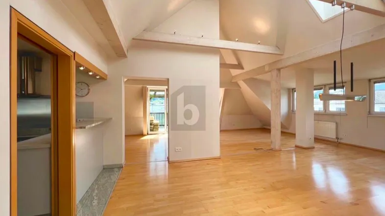 Heller, offener Wohnbereich mit Holzbalken, Parkettboden und Dachfenstern, mit Zugang zu einem Balkon.