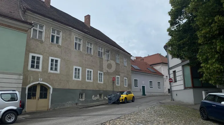 Historisches Gebäude an einer Kopfsteinpflasterstraße mit traditionellen Fenstern und Putzfassade.
