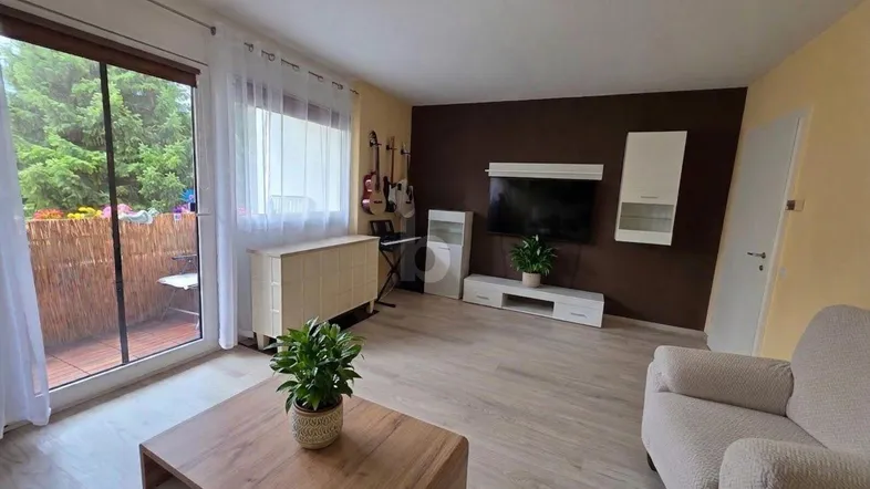 Helles Wohnzimmer mit Laminatboden, moderner Einrichtung und direktem Zugang zum Balkon mit Grünblick.