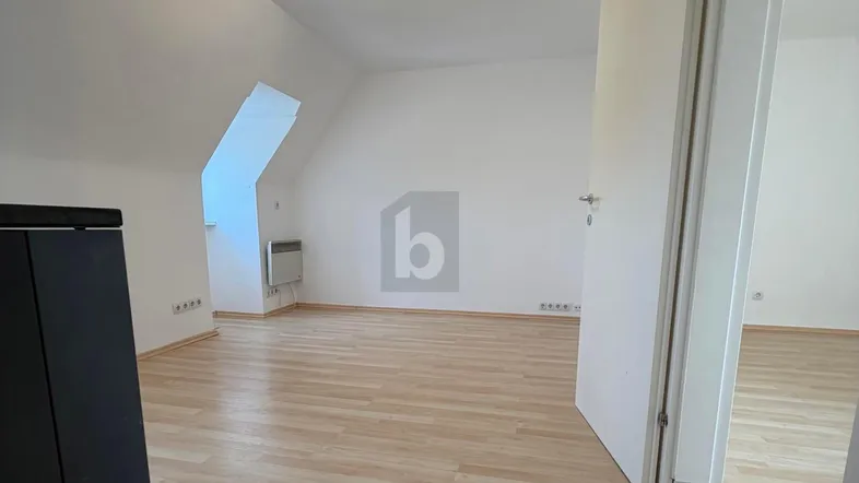 Helles Zimmer im Dachgeschoss mit Laminatboden, schrägen Wänden und einem Fenster in der Dachschräge.