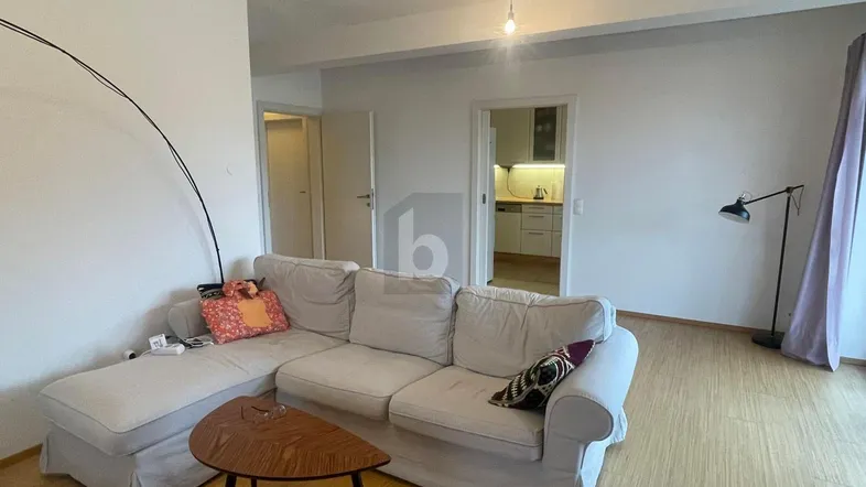 Helles Wohnzimmer mit beigem Ecksofa, Holzboden und offenem Zugang zur Küche.