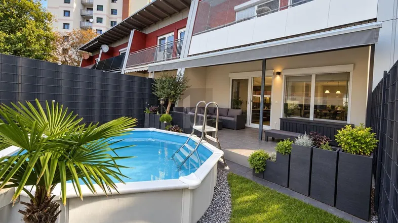 Gepflegter Gartenbereich mit kleinem Aufstellpool, Rasenfläche und überdachter Terrasse mit Sitzgelegenheiten.