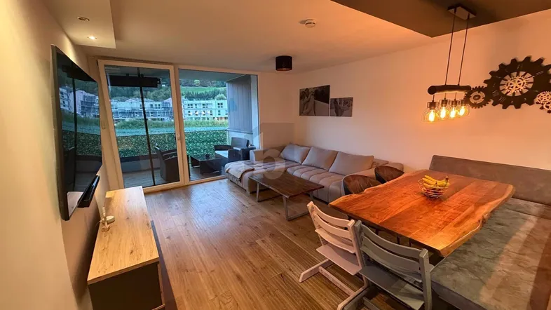 Moderner Wohn-Essbereich mit Holzboden, gemütlichem Sofa und Zugang zu einem Balkon mit Aussicht.