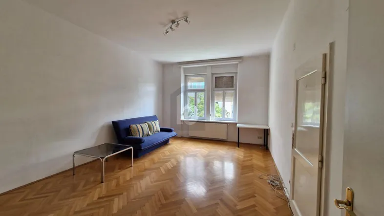Helles Wohnzimmer mit Fischgrätparkett, einem blauen Sofa und einem Fenster mit Blick nach draußen.