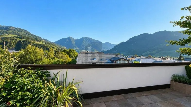 Geräumige Terrasse mit Fliesenboden, Pflanzen und einem weiten Blick auf die umliegende Berglandschaft.