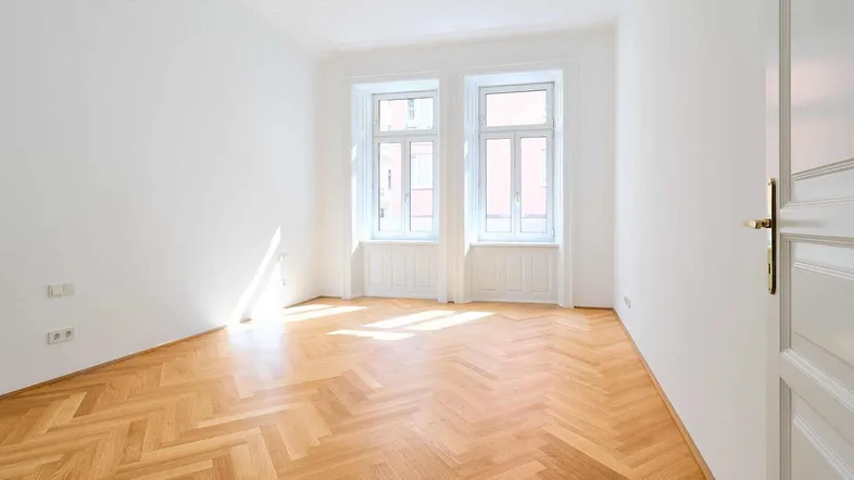 Helles Zimmer mit Fischgrätparkett und großen Fenstern, das viel Tageslicht hereinlässt.