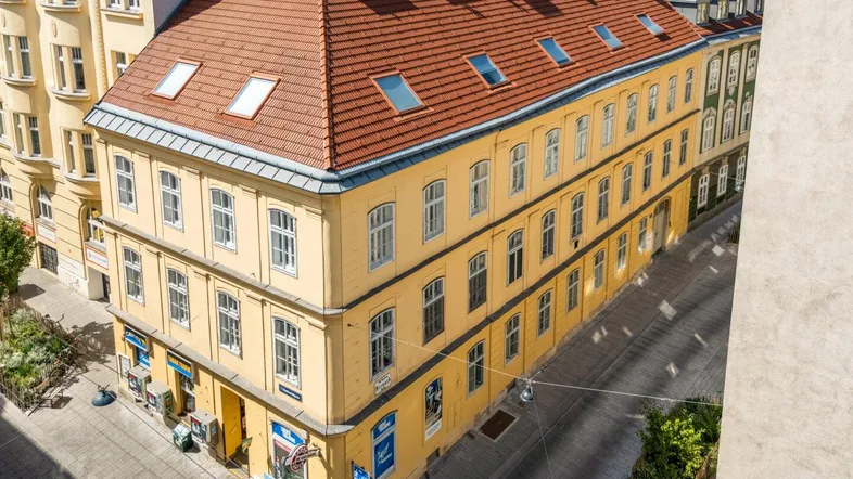 Gebäudeansicht von oben mit gelber Fassade, roten Ziegeldächern und Dachfenstern.