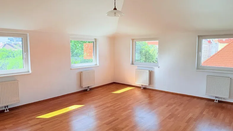Helles, leeres Zimmer mit Holzparkettboden, mehreren Fenstern und Heizkörpern, ideal für Wohn- oder Schlafbereich.