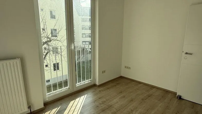 Helles Zimmer mit Laminatboden und Zugang zu einem französischen Balkon.
