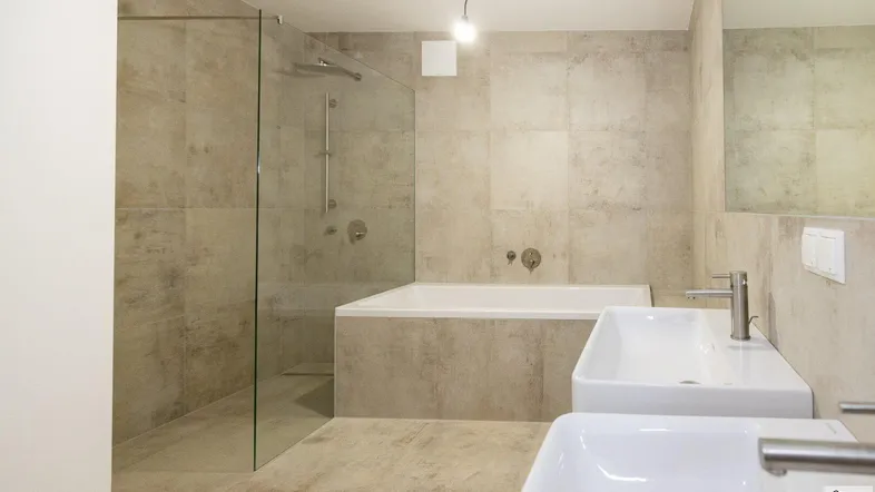 Modernes Badezimmer mit begehbarer Dusche, Badewanne und zwei Waschbecken, alles in hellen Fliesen gehalten.