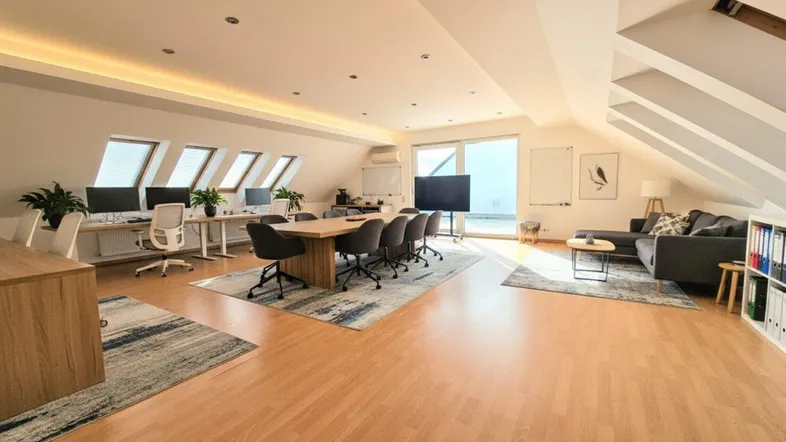 Großes, modernes Büro im Dachgeschoss mit mehreren Arbeitsplätzen, Konferenztisch und gemütlicher Lounge-Ecke.