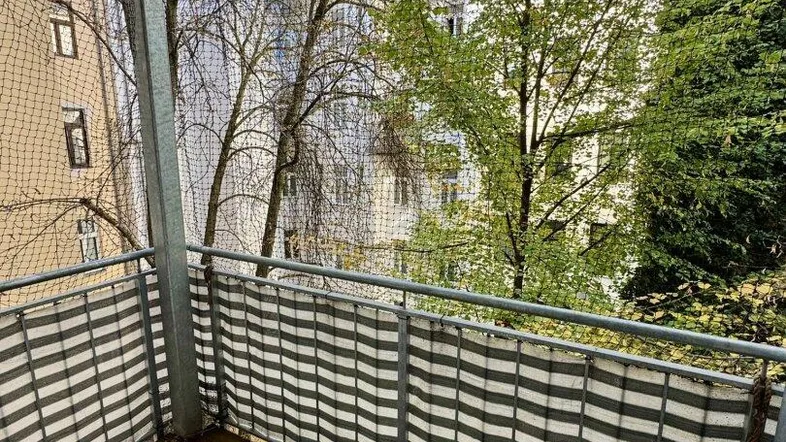 Balkon mit Holzboden, Schutznetz und Blick auf Bäume und umliegende Gebäude.