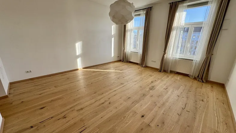 Sonniges Zimmer mit hellem Holzparkettboden und großen Fenstern, die viel Tageslicht hereinlassen.