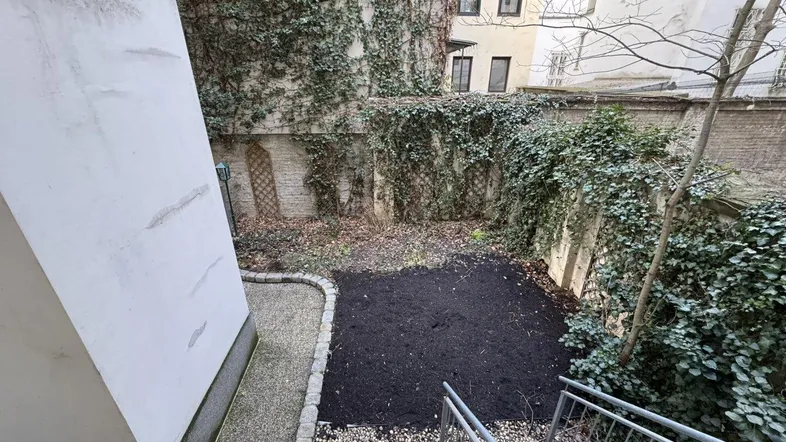 Begrünter Innenhofgarten mit Kiesweg und Treppenzugang, umgeben von bewachsenen Mauern.