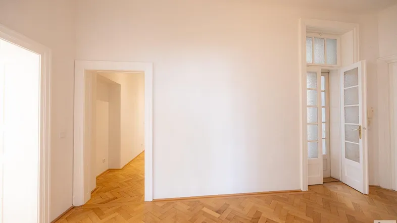 Helles Zimmer mit Fischgrätparkettboden und mehreren Türen, die zu anderen Räumen führen.