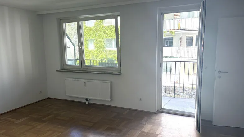 Helles Zimmer mit Parkettboden und Zugang zu einem Balkon, ideal als Wohn- oder Schlafbereich.