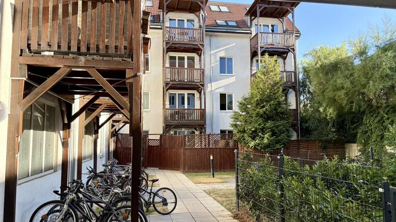 Außenansicht eines Mehrfamilienhauses mit Holzbalconen, Fahrradstellplätzen und begrüntem Innenhof.