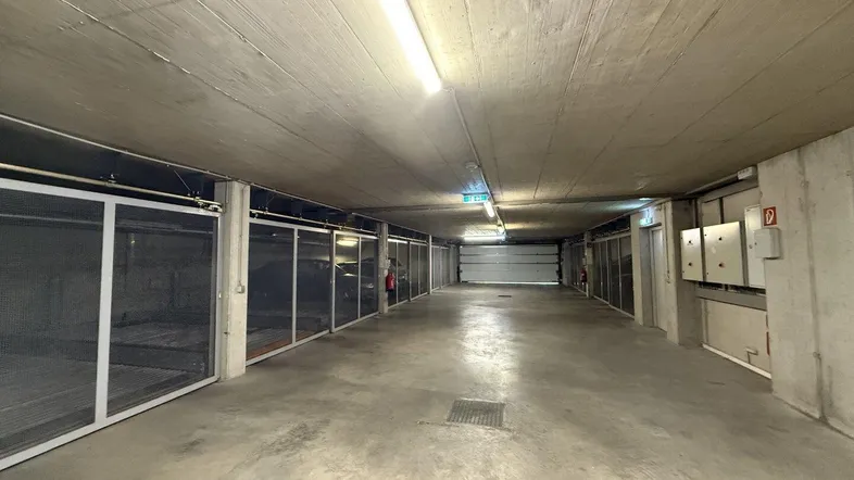 Geräumige Tiefgarage mit Betonwänden und Gitterboxen für Fahrzeuge und zusätzlichem Stauraum.