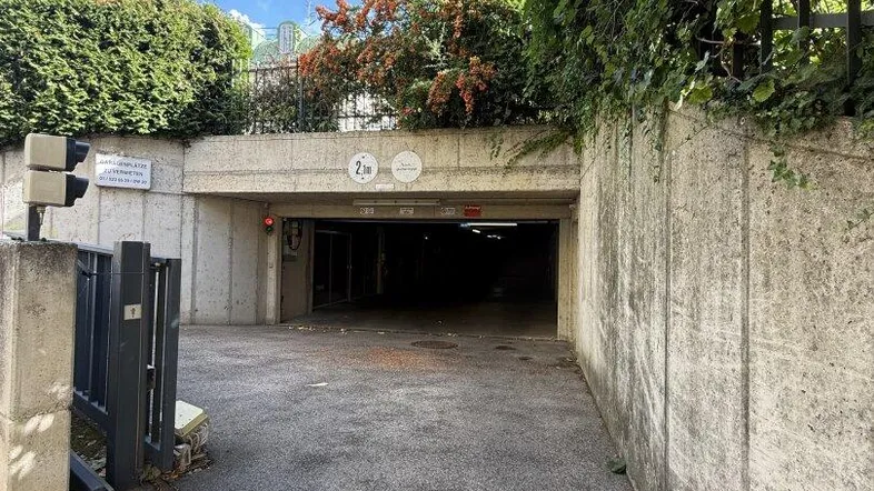 Einfahrt zur Tiefgarage mit Betonwänden, umgeben von üppigem Grün und Kopfsteinpflaster.