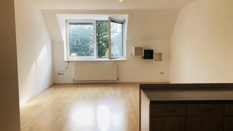 Helles Zimmer mit Dachschräge, großem Fenster und Heizkörper, ideal als Wohnbereich nutzbar.