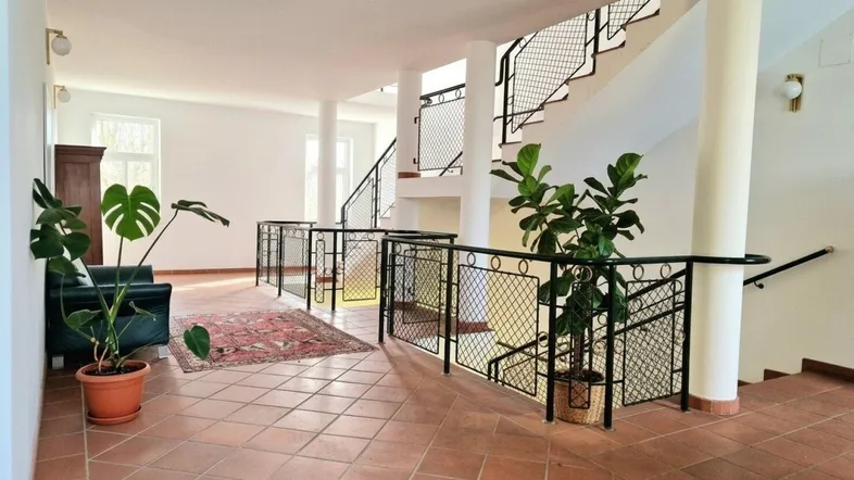 Geräumiger Flur mit Terrakottafliesen, Säulen und einer Treppe mit schmiedeeisernem Geländer.