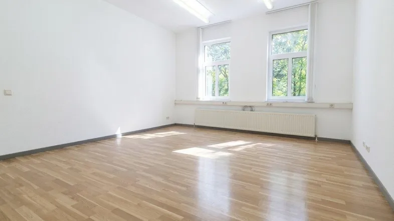 Heller Raum mit Holzparkett, weißen Wänden und zwei Fenstern, die viel Tageslicht hereinlassen.
