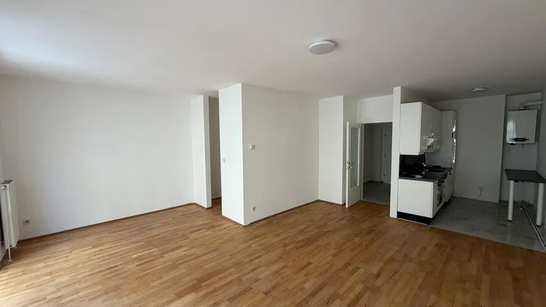 Helles Wohnzimmer mit Holzboden und integrierter, moderner Küchenzeile in Weiß.